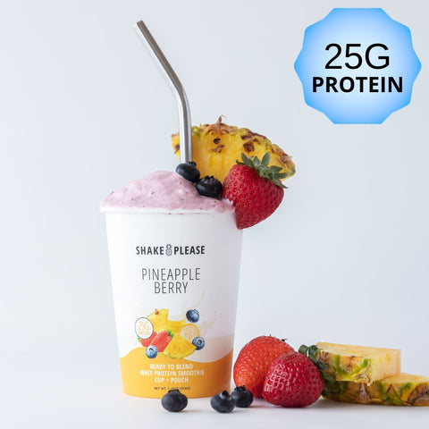 Premade pineapple berry protein smoothie in a white cup with a yellow lid labeled 25g protein, with fresh pineapple chunks, strawberries, blueberries, and banana slices around it.
